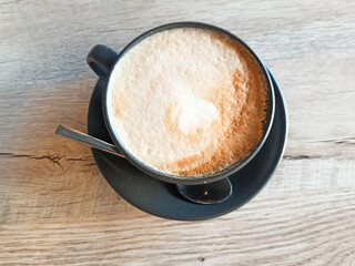 Close up cup of coffee with spoon on wooden background, cappuchino with shaked milk, view from the top, drinks topic