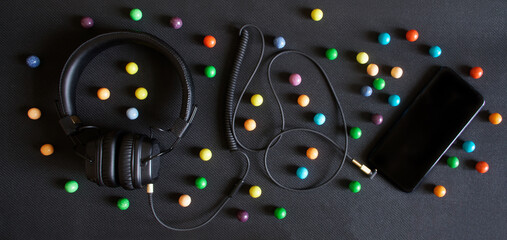 Wired headphones with ear pads and a smartphone lie on a black background next to colorful balls.