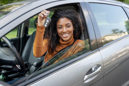 Black woman holding up car key to her first new car. Customer satisfaction