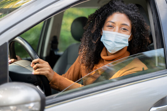 African woman with curly hair with face mask on sitting and driving car. Prevention from spreading corona virus