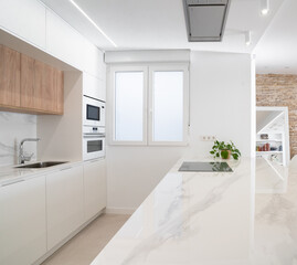 Cocina abierta moderna de diseño de color blanco y con armarios de madera con encimera de mármol y campana extractora integrada en el techo en casa de lujo