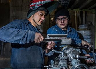 Waist up portrait of two welders while working in garage. Male worker with special protective mask operating lathe machine - metalworking industry concept. 