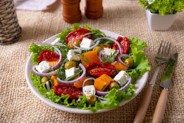 Warm salad with pumpkin, feta cheese, sun-dried tomatoes, olives, arugula and red onion. Close-up.