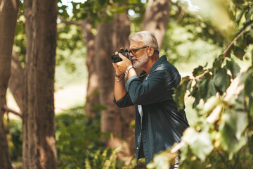 A modern old man with a camera in his hands on a walk in the forest.