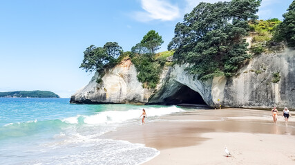Famous beach of Cathedral Cove in New Zealand on a sunny day. Tourists go swimming in the clear,...
