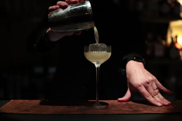 Bartender pouring the drink into cocktail glass