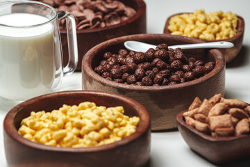 Bowls with different sorts of breakfast cereal products and glass of milk