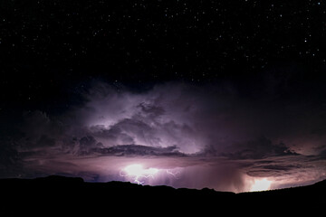 Powerful lightning storm in the American Southwest. One sees the silhouette of the hills on bottom, and moving up from there the lightning, cumulonimbus and the starry sky above. 