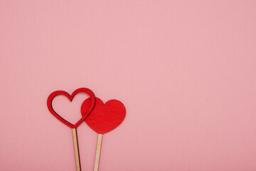 Two red wooden love hearts on a pink background