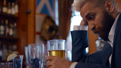 Young businessman sitting at bar drinking beer feeling thoughtful