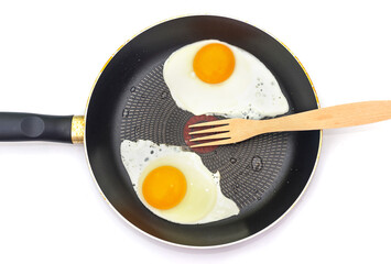 Fried eggs in a frying pan with a wooden fork isolated on white.