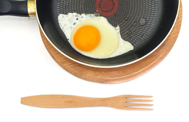 Wooden fork and fried egg in a frying pan on a white background.