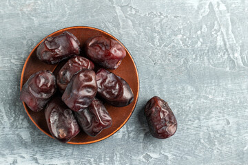 Dried organic date fruits in a plate on a gray background top view