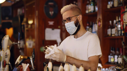 Bartender wearing face mask and gloves cleaning empty glass