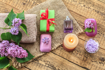 Towels, soap, gift, candle and lilac flowers on wooden background.