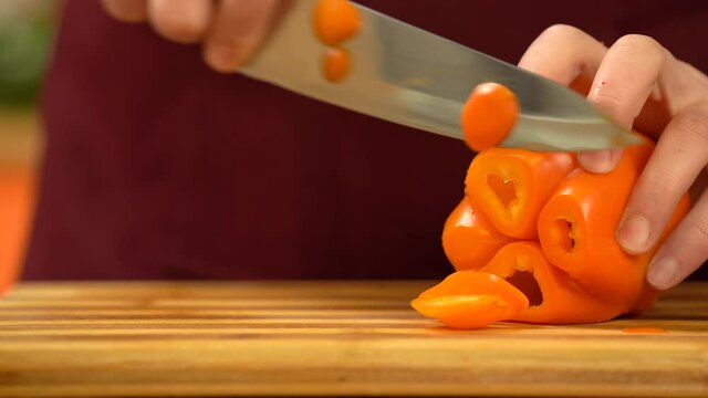 Chef cutting vegetables on a wooden board. Man's hand cutting orange, big, fresh pepper  in kitchen. Chef slicing fresh vegetables in kitchen. Healthy Food Concept. Preparing Vegetable for cooking. Hi