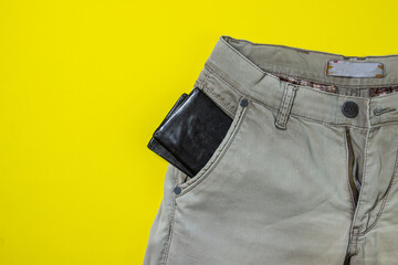 The wallet is sticking out of my pants pocket. Male accessory. Black wallet. Clothes on a yellow background.