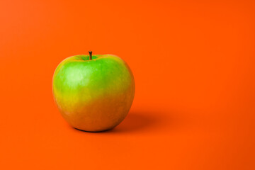 A green apple on an orange background. Minimalism and copy space. The concept of healthy eating and weight loss