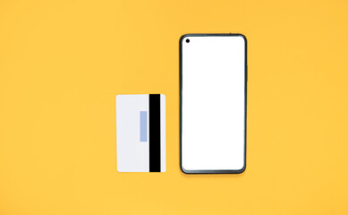 Smartphone with white screen mockup and gray bank card on bright yellow background. Concept of online shopping using the phone. copy space for text. view from above. Flat lay