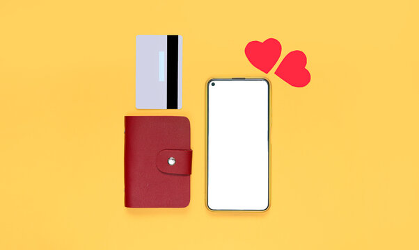 Smartphone with white screen mockup, wallet, credit card, hearts on yellow background. Concept of shopping for gifts on the internet using the phone on valentine's day. copy space for text. top view. 