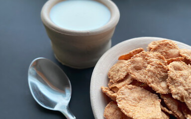 Breakfast cereals, multi-grain flakes in a clay plate and milk in clay cup on a beautiful black background.  Food concept.