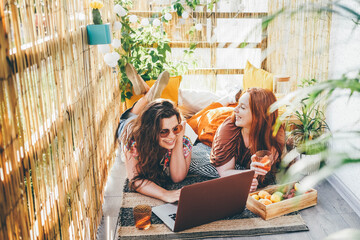 joyful girls use modern laptop and drink delicious natural cocktails spending time together on...