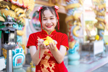Portrait beautiful smiles Cute little Asian girl wearing red traditional Chinese cheongsam decoration holding golden money bag for Chinese New Year Festival at Chinese shrine in thailand