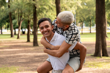 Young gay guy giving a piggyback ride in a public park