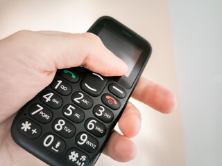 Hand palm holding big push button, simple mobile phone for seniors.