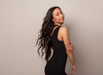Naklejka premium Beautiful young woman with long shiny black hair and natural make-up posing in dress on grey background 