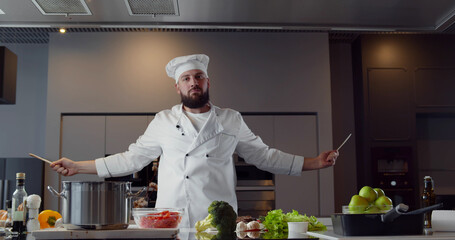 Man chef having fun and doing karate with kitchen utensils looking at camera