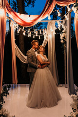 Night ceremony. The bride and groom congratulate each other against the background of the lights of the wedding arch.