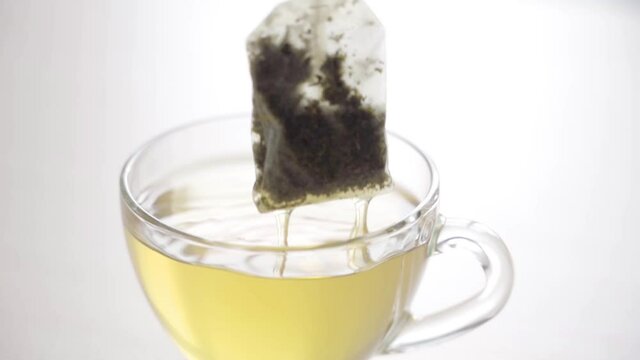 Tea Bag in a Tea Cup. Brew Green Tea in a Mug. White Background, Slow Motion