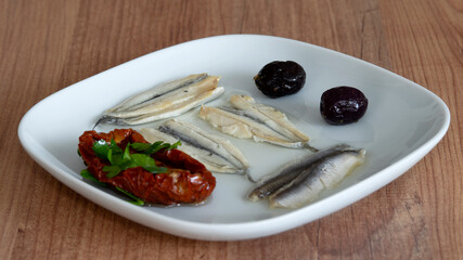 Pickled anchovies, dried tomatoes and olives on a plate.