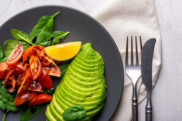 Vegetable salad with tomatoes, avocado and spinach in a grey plate. Healthy lifestyle concept