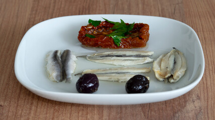 Pickled anchovies, dried tomatoes and olives on a plate.