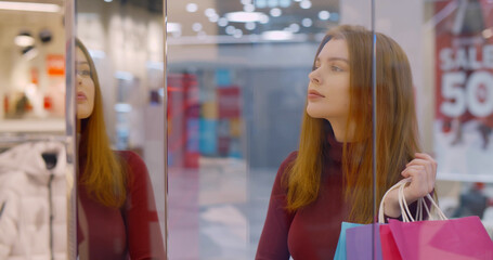 Young woman holding bags with purchase staring at shop window