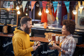friends talking and laughing while eating sandwiches in front of fast food service