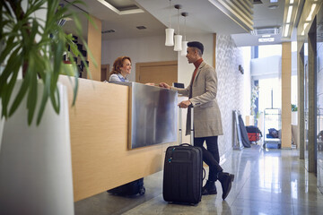 young  afro-american male paying with card to a friendly female caucasian at reception desk