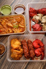 Top view of traditional Indian food in a plastic box on a wooden table. Indian fast food delivery at home. Eat at home.