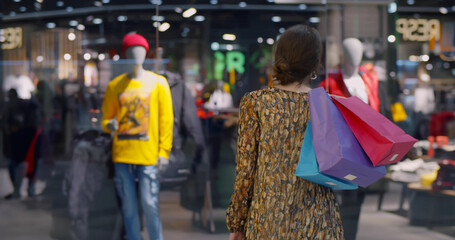 Young woman in protective mask looking at shop windows in shopping mall