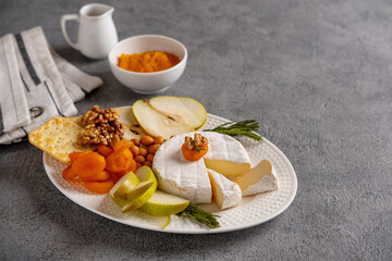 Brie cheese with nuts, pear slices and dried apricots. Camembert cheese. Brie cheese or Camembert cheese  on a wooden board. Tasty cheese starter.