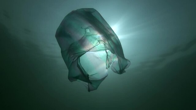 Plastic pollution, used blue plastic bag slowly drifting underwater in the sun's rays. Plastic debris underwater. Plastic garbage environmental pollution problem. Slow motion, backlight. Black Sea.