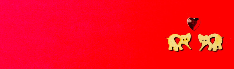 Two enamored wooden elephants with a crystal heart on a red background. Long love background. Valentine's day and wedding.