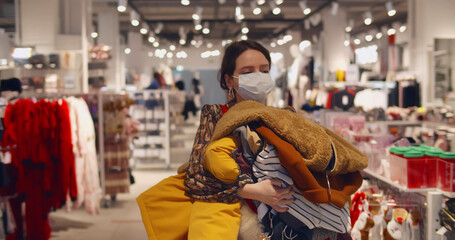 Fototapeta premium Woman shopping in fashion store wearing face mask carrying clothes to fitting room