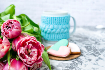 Bouquet of pink tulips, a cup of tea, and sweet gingerbread cookies in the shape of a heart on a light background. Copy space. Spring holiday concept, Valentine's Day.
