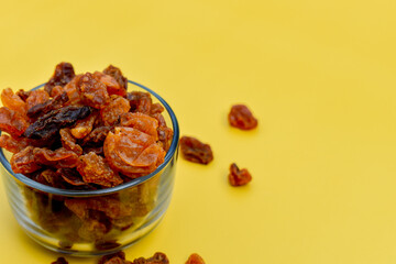 a group of dry brown grapes in a glass bowl in yellow background