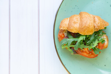 Croissant with rocket salad and vegetables on a ceramic dish on a wooden table