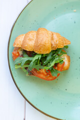 Croissant with rocket salad and vegetables on a ceramic dish on a wooden table