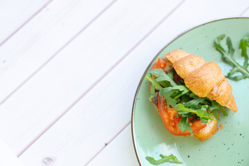 Croissant with rocket salad and vegetables on a ceramic dish on a wooden table